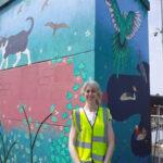 The artist, Caroline Daly, stands in front of her new mural at Chorlton tram station